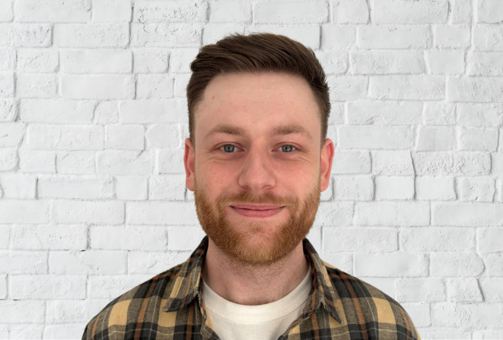 Man smiles at the camera. He has a beard and short brown hair.