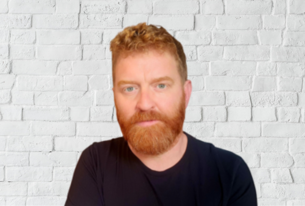 Man looking at camera. He has red hair and a beard.