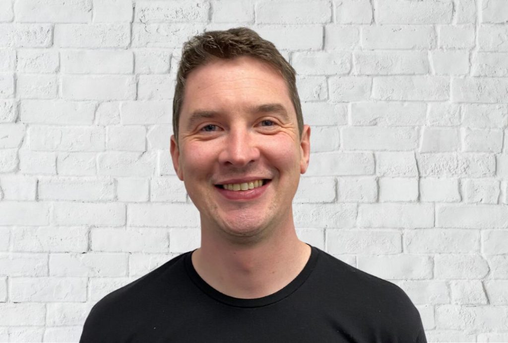 A man with short brown hair smiles at the camera.