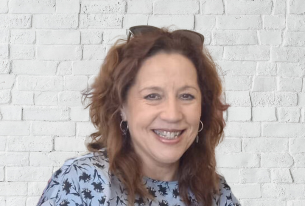 Woman smiles at the camera. She is wearing a blue dress.