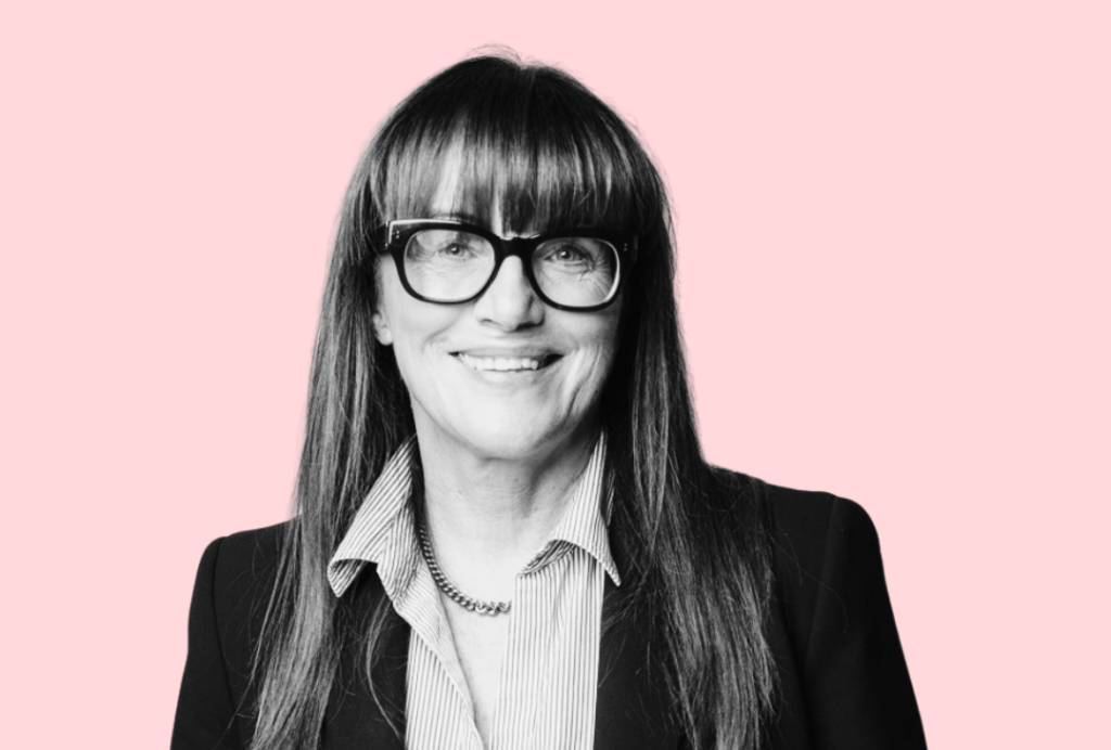 A woman smiles at the camera. She has long hair and glasses.