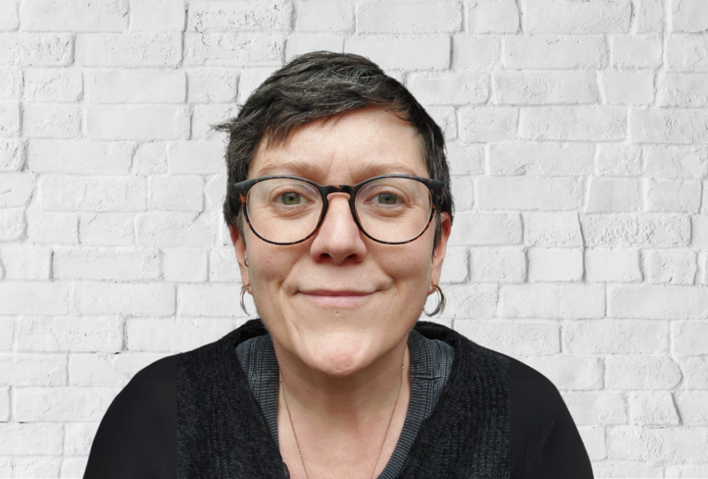 A woman smiles at the camera. She has short dark hair and is wearing glasses.